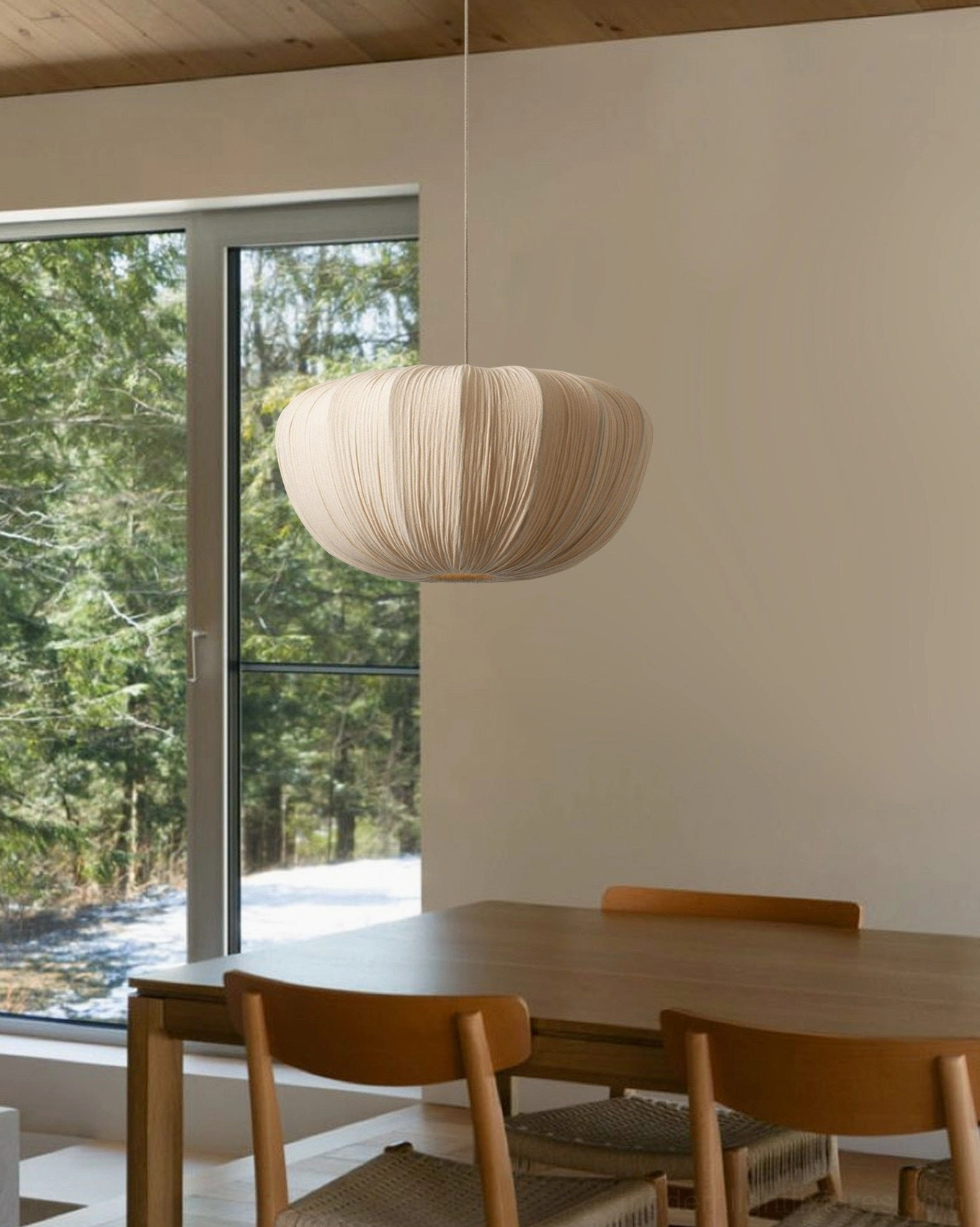 Beige pleated fabric pendant light three-quarter view in natural dining room with wooden furniture and forest view window