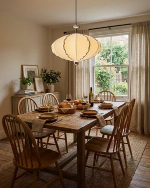 Modern cream pleated pendant light installed above dining table in warm minimalist dining room with black scalloped trim detail visible