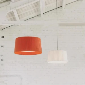Two cylindrical pleated pendant lamps in orange and white shades displayed on industrial brick wall