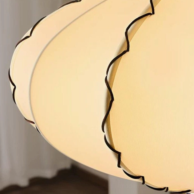 Extreme close-up detail of cream linen-look fabric with black wavy scalloped trim pattern on pleated pendant light shade