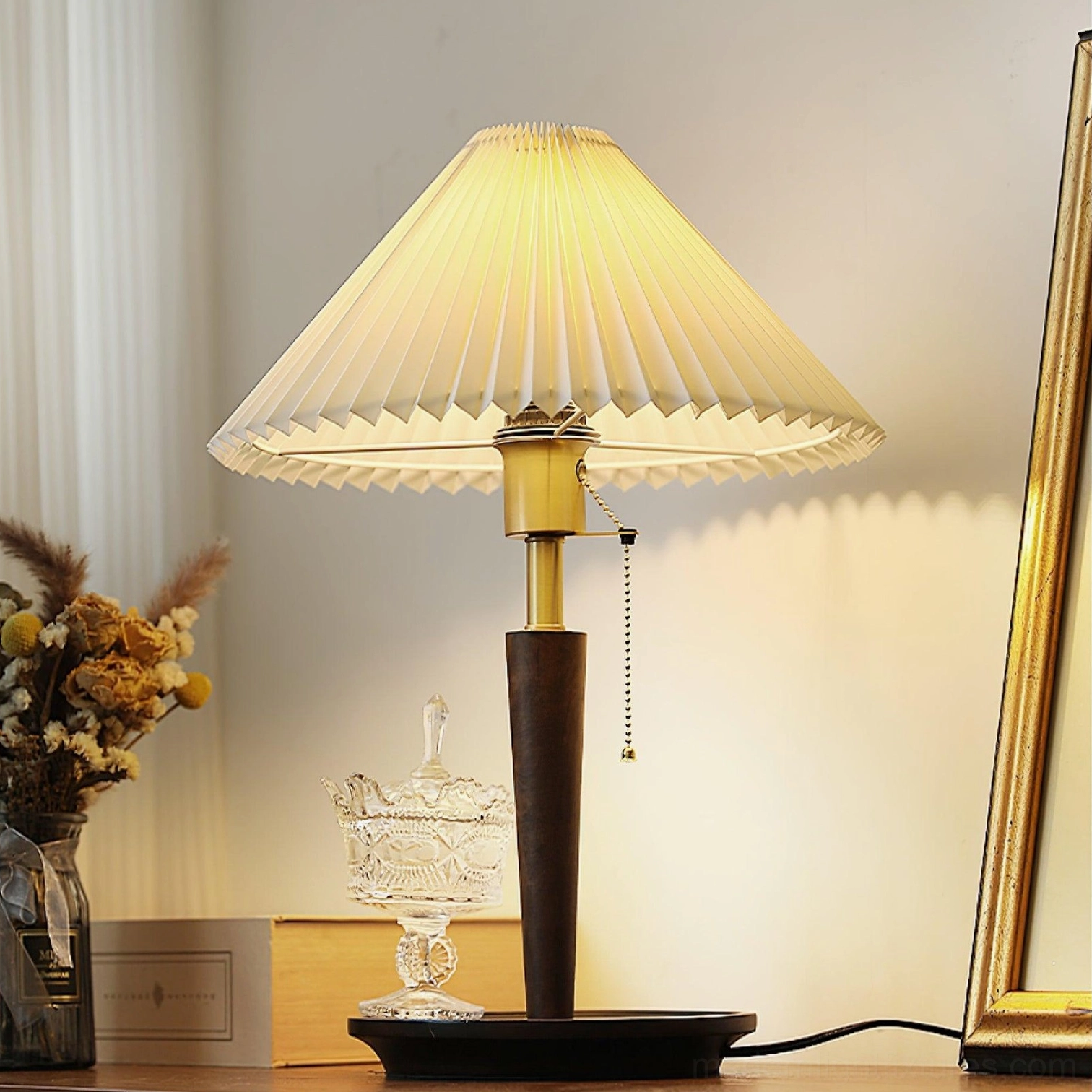 Suki pleated table lamp displaying soft warm light, styled on dresser with dried flowers and glassware, side angle