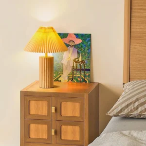 Pleated table lamp positioned on bedroom nightstand, creating warm ambient lighting with interior artwork and Japandi décor