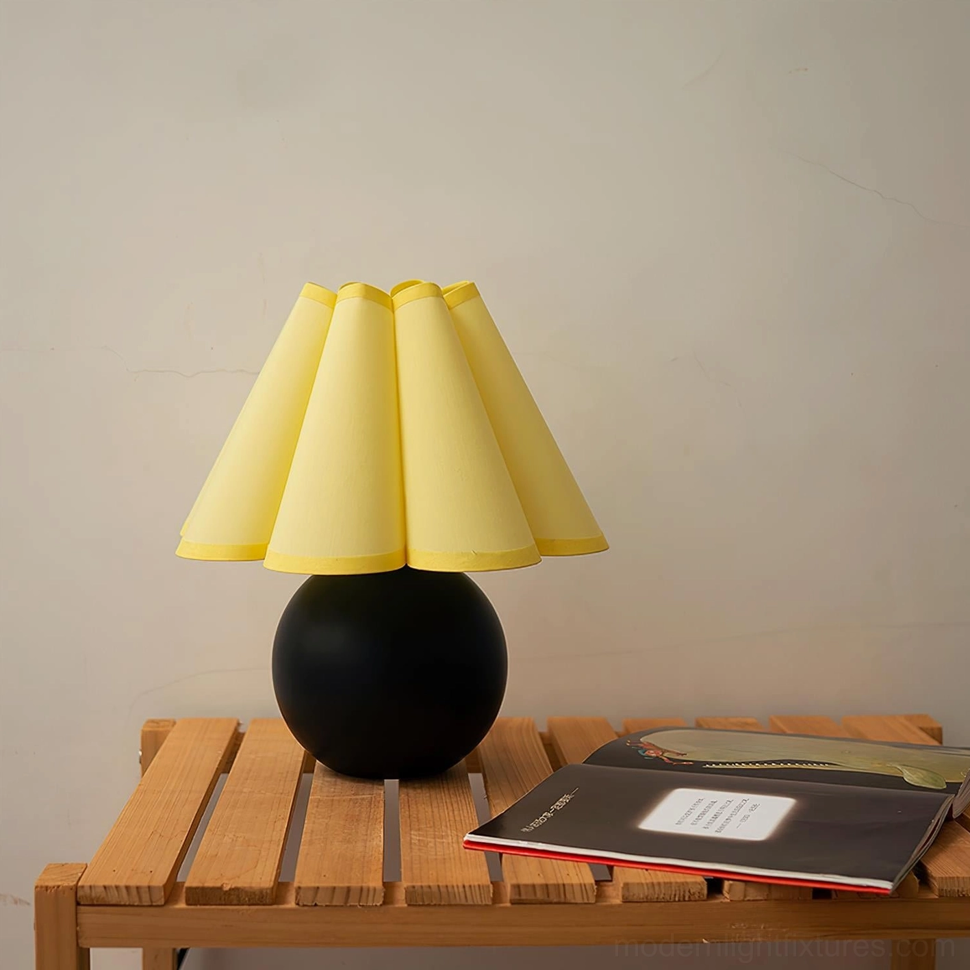 Contemporary pleated table lamp with black ceramic base and warm yellow shade displayed on wooden side table in home setting