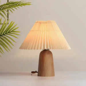 Lit pleated table lamp creating warm glow on bedside table with tropical plant decor, Scandinavian bedroom lighting