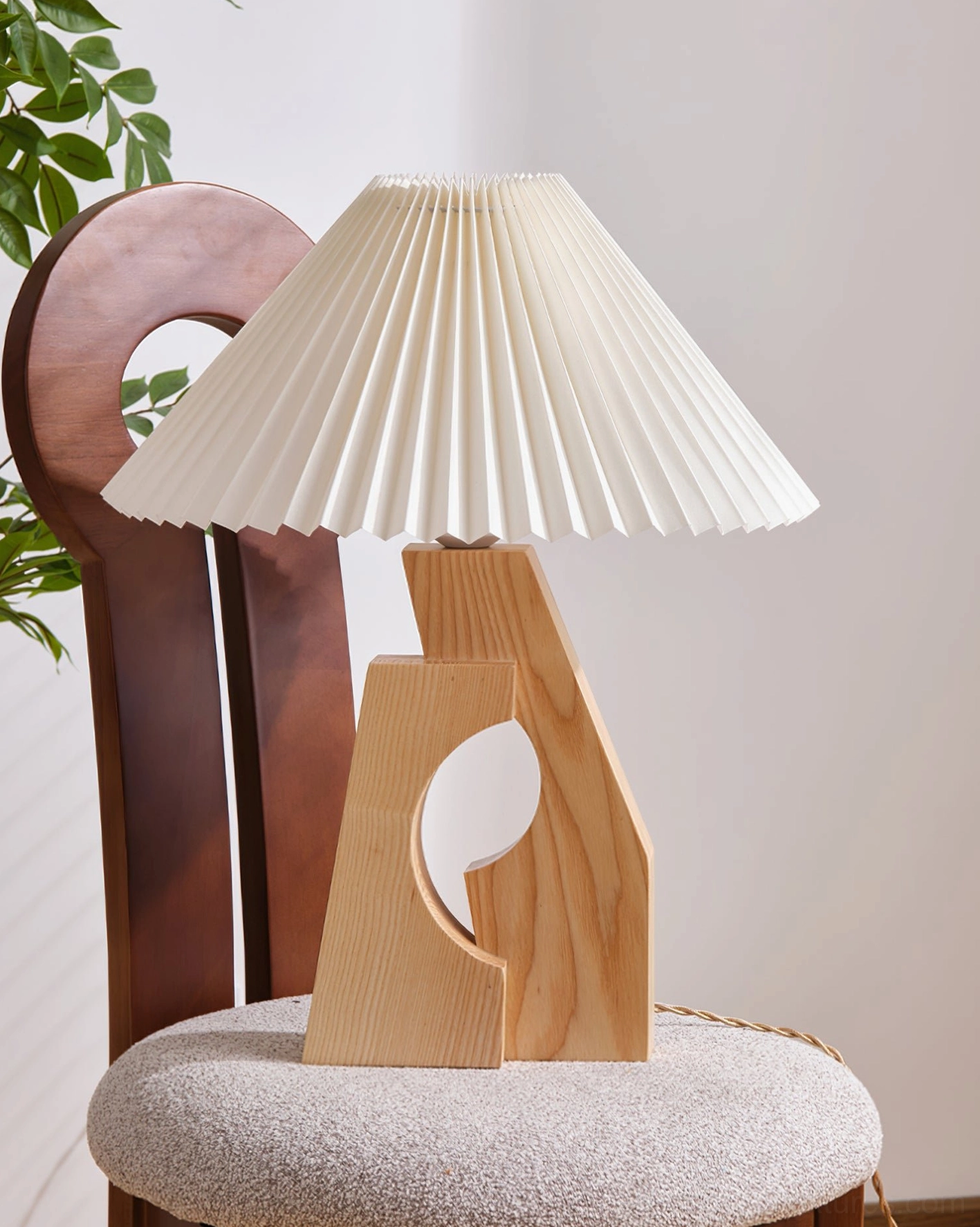 Pleated white fabric table lamp with natural wood base side view, styled with upholstered dining chair and green plants