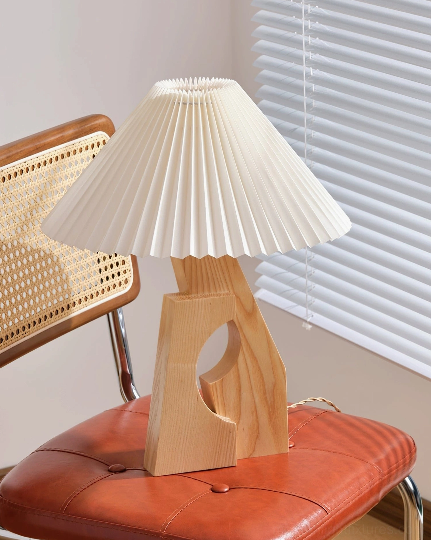 Modern pleated white shade table lamp with natural wood base, three-quarter view with retro leather rattan chair