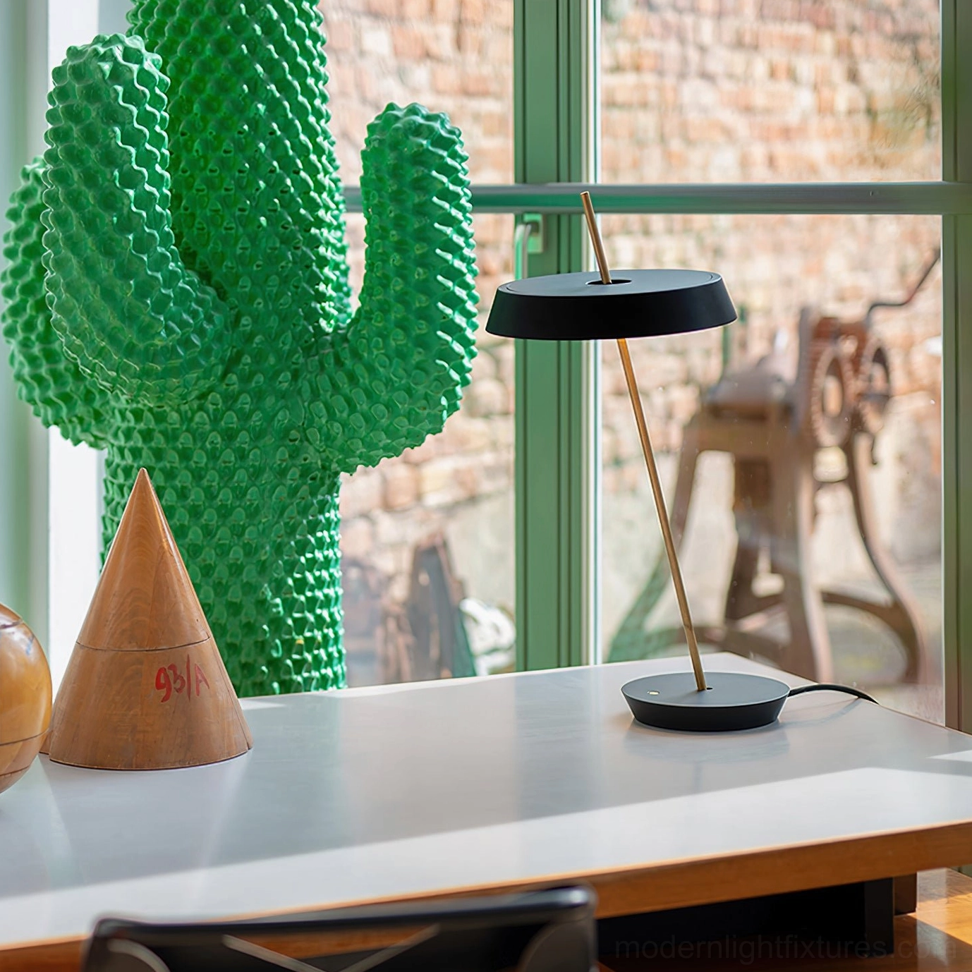 Black Poldina modern disc table lamp in contemporary home office with cactus and brick window backdrop