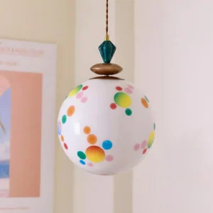 Polka dot pendant light with bronze and teal hardware, three-quarter angle against art print backdrop