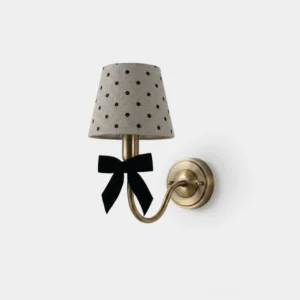Polka dot wall sconce with black velvet bow and tapered linen shade featuring classic black polka dots, frontal studio view with brass metal backplate and curved arm