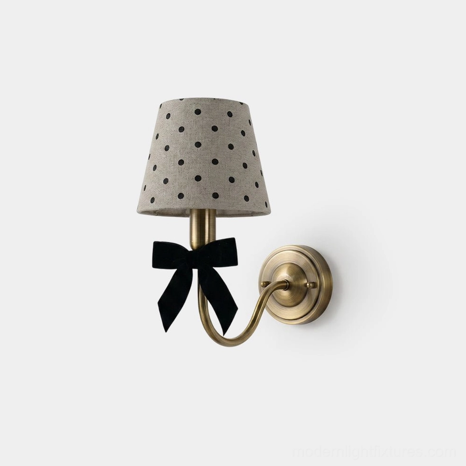 Polka dot wall sconce with black velvet bow and tapered linen shade featuring classic black polka dots, frontal studio view with brass metal backplate and curved arm