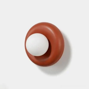 Pop wall sconce with terracotta resin donut body and opal white glass globe, front view on neutral studio background