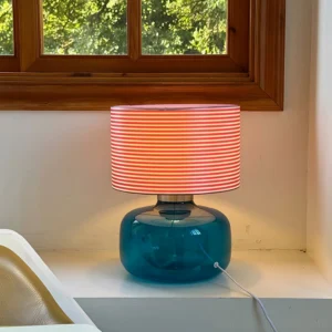 Popello table lamp lit on windowsill with blue glass base creating ambient lighting in natural daylight