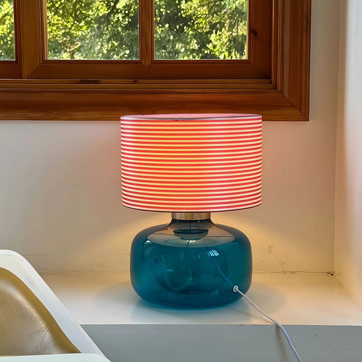 Popello table lamp lit on windowsill with blue glass base creating ambient lighting in natural daylight
