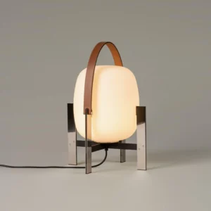 Illuminated portable metal table lamp with frosted glass shade displaying warm light diffusion and polished metal stand with exposed power cord
