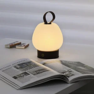 Modern portable table lamp providing warm white light on home office desk with magazines and decor