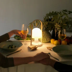 Rechargeable portable table lamp creating warm ambient lighting for intimate dinner setting overhead view