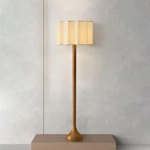 Lit Portillo fabric shade floor lamp emitting warm ambient light, displayed on wooden plinth with textured wall backdrop