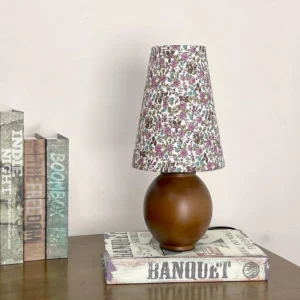 Positano table lamp with walnut wood base and floral shade displayed on wooden surface with books