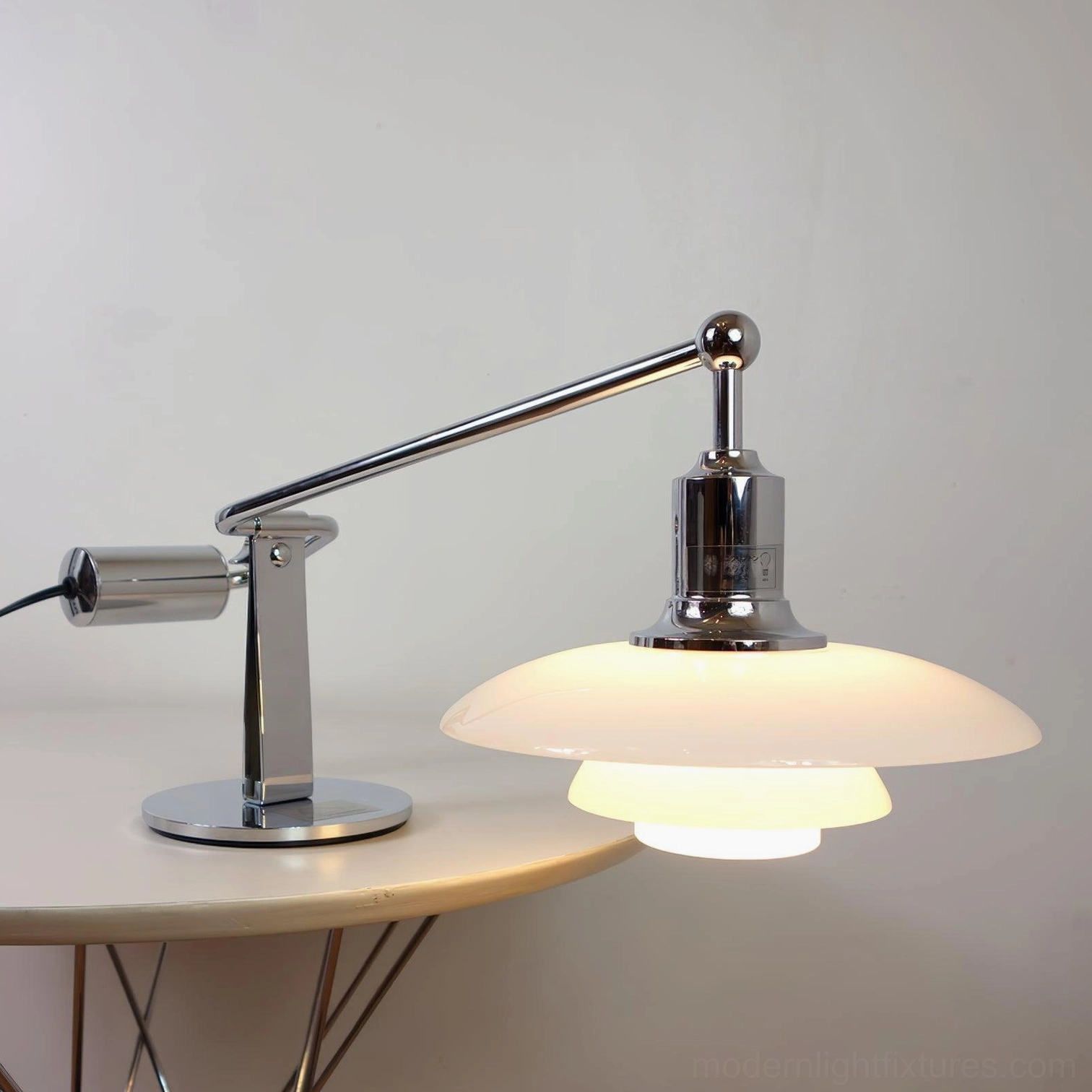 Poul wide shade modern table lamp with full chrome body on side table emitting warm glow
