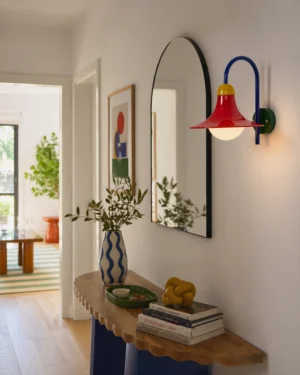 Primora modern wall sconce mounted in residential entryway beside decorative arched mirror for ambient lighting and artistic wall accent