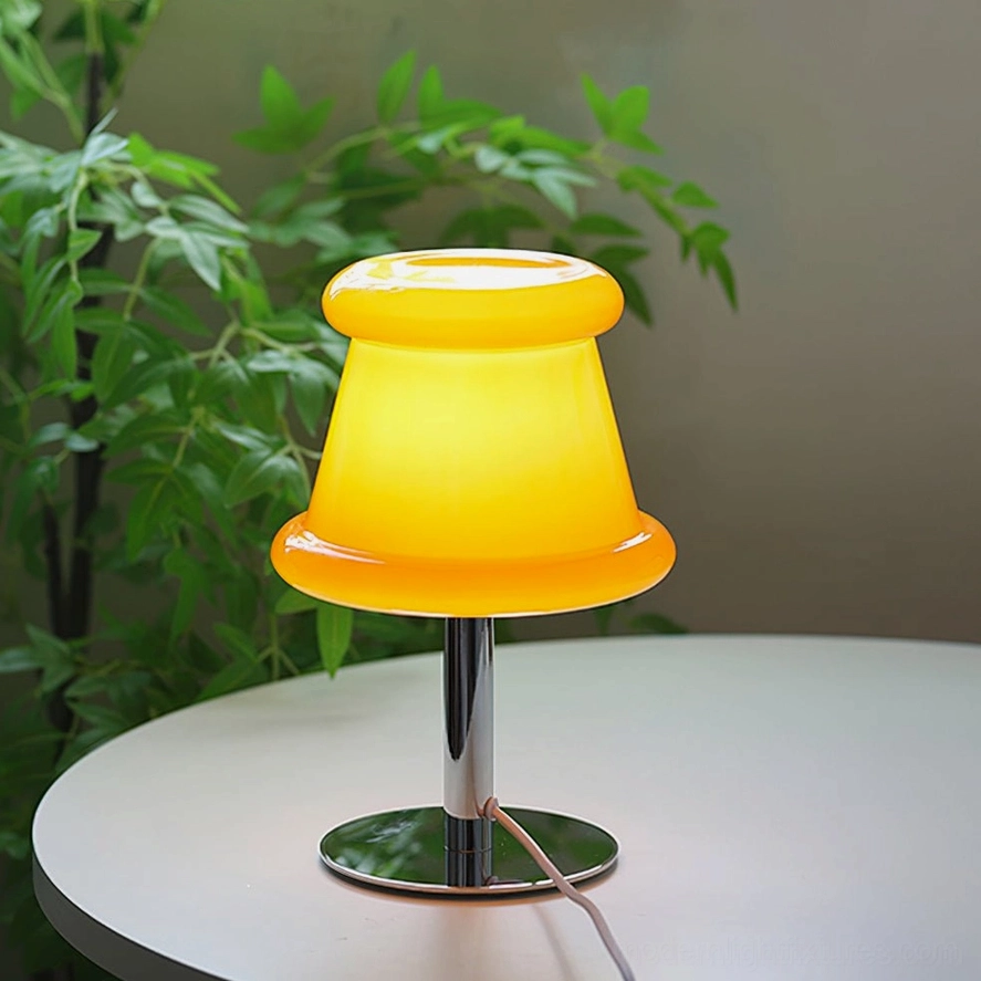 Lit amber orange pudding glass table lamp casting warm diffused glow on side table with green plant decor background