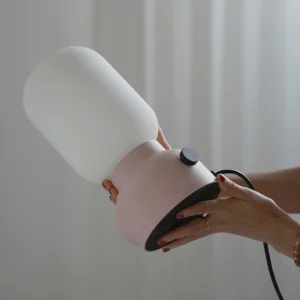 Close-up detail of Pulg table lamp showing dimmer knob, detachable frosted glass shade, and built-in power socket on ceramic base