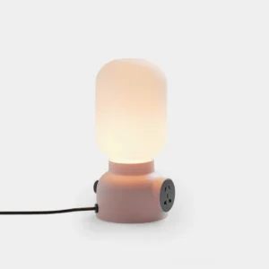 Pulg modern table lamp with integrated power outlet and frosted glass shade, front studio view showing pink ceramic base