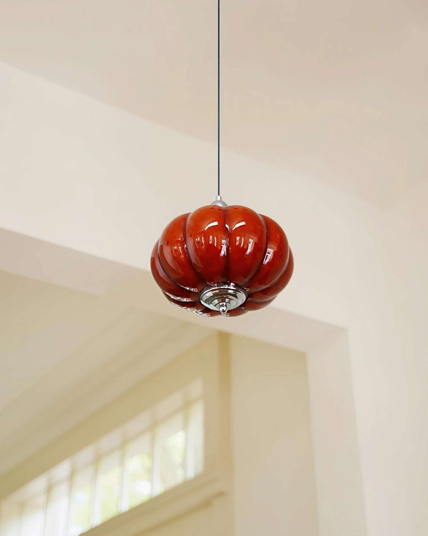 Red pumpkin-shaped glass pendant light with black suspension cable in residential entryway