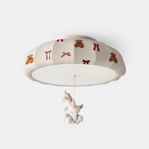 Front close-up view of whimsical pumpkin ceiling light with off-white fabric shade featuring bear and bow prints, suspended unicorn ornament decoration