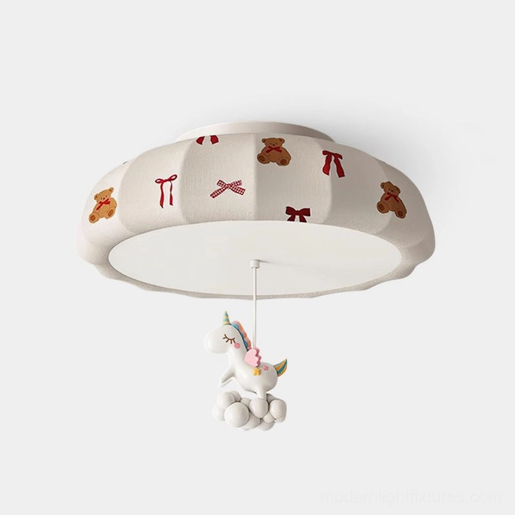 Front close-up view of whimsical pumpkin ceiling light with off-white fabric shade featuring bear and bow prints, suspended unicorn ornament decoration