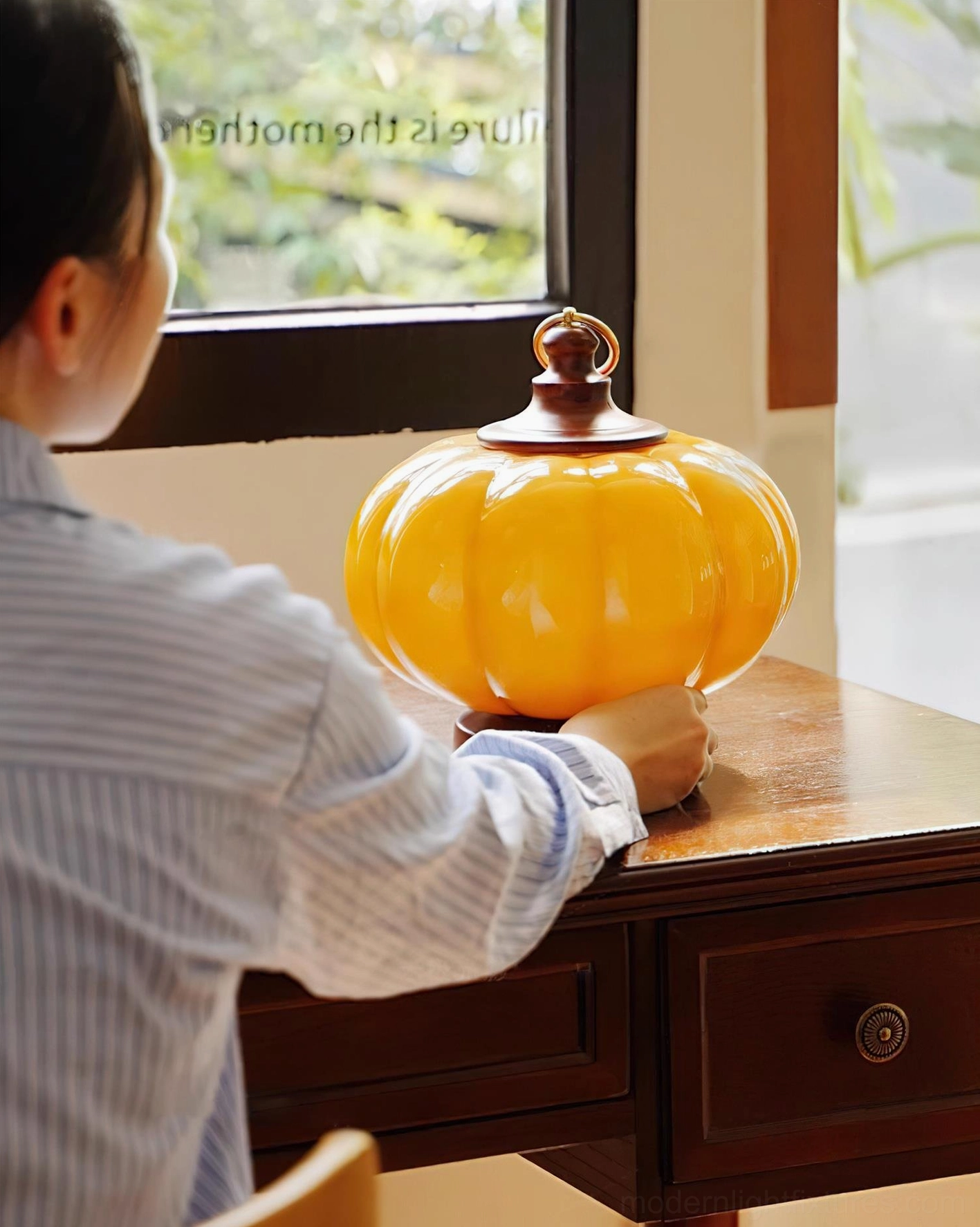 Pumpkin table lamp over-shoulder rear view placed on dark wooden desk by window in home office setting