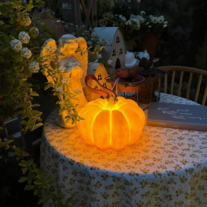 Glowing pumpkin LED table lamp in outdoor garden dining setup creating warm ambient lighting with floral décor