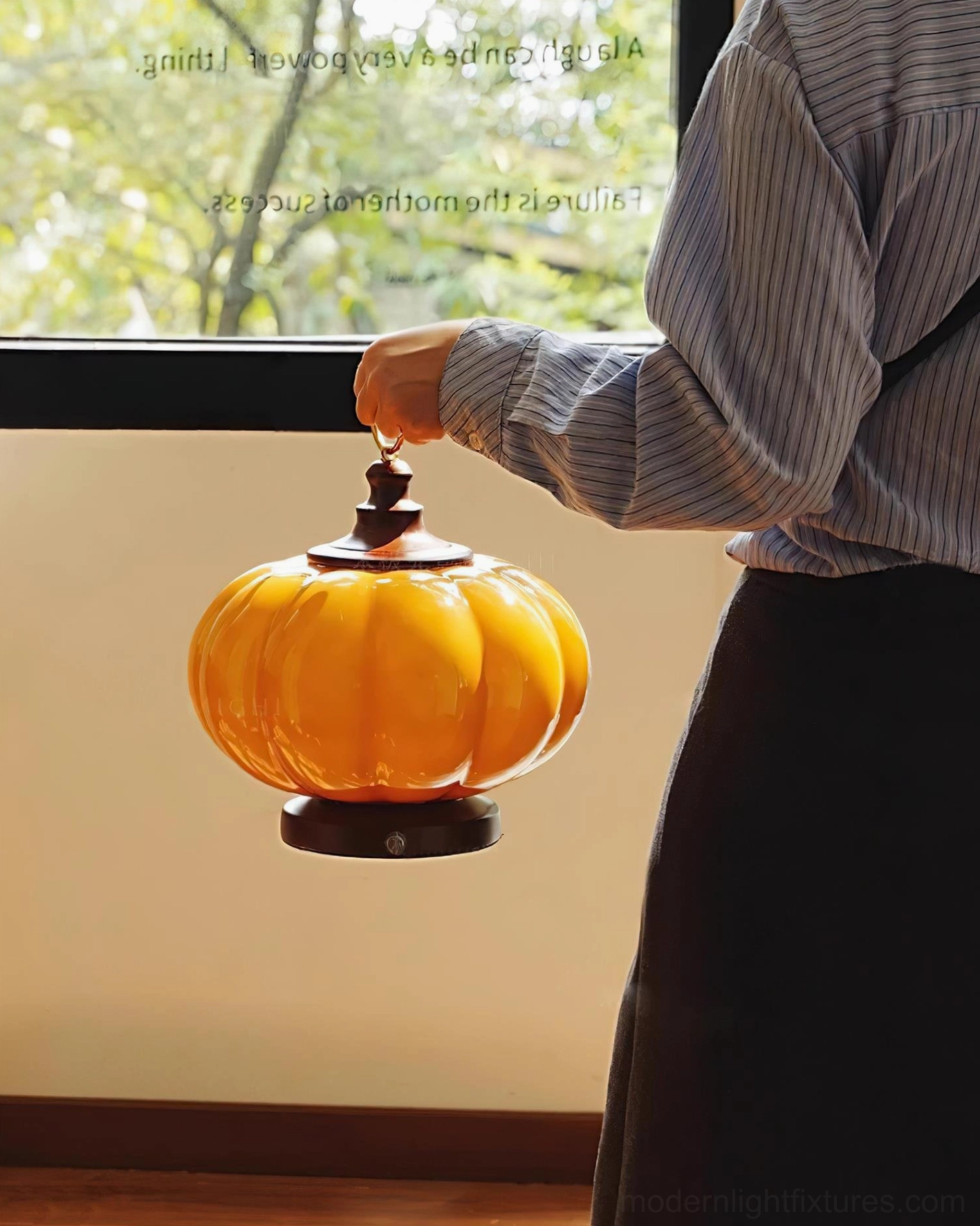 Pumpkin table lamp side rear view held by hand in striped work shirt by home window demonstrating portability and accessibility
