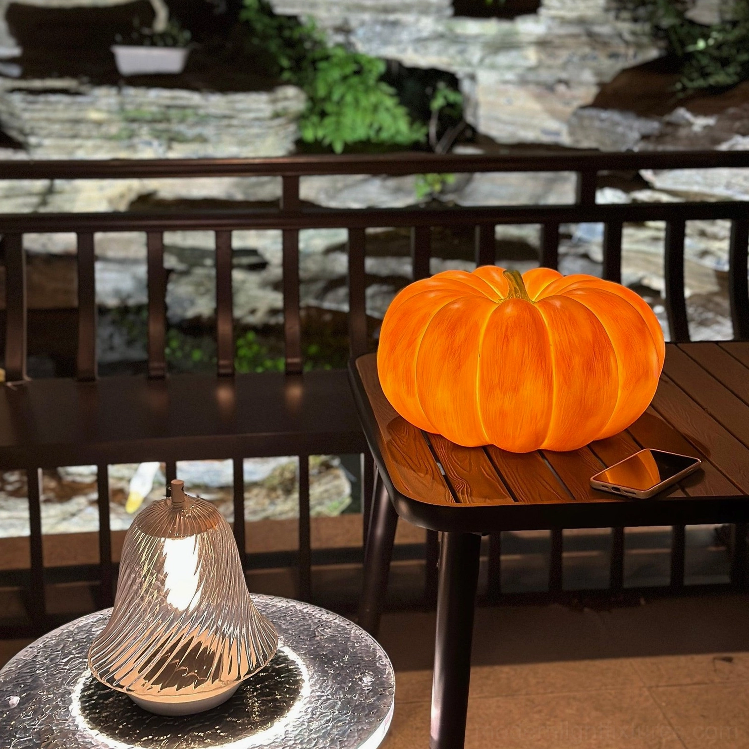 Large pumpkin table lamp glowing orange on wooden terrace side table garden seating area