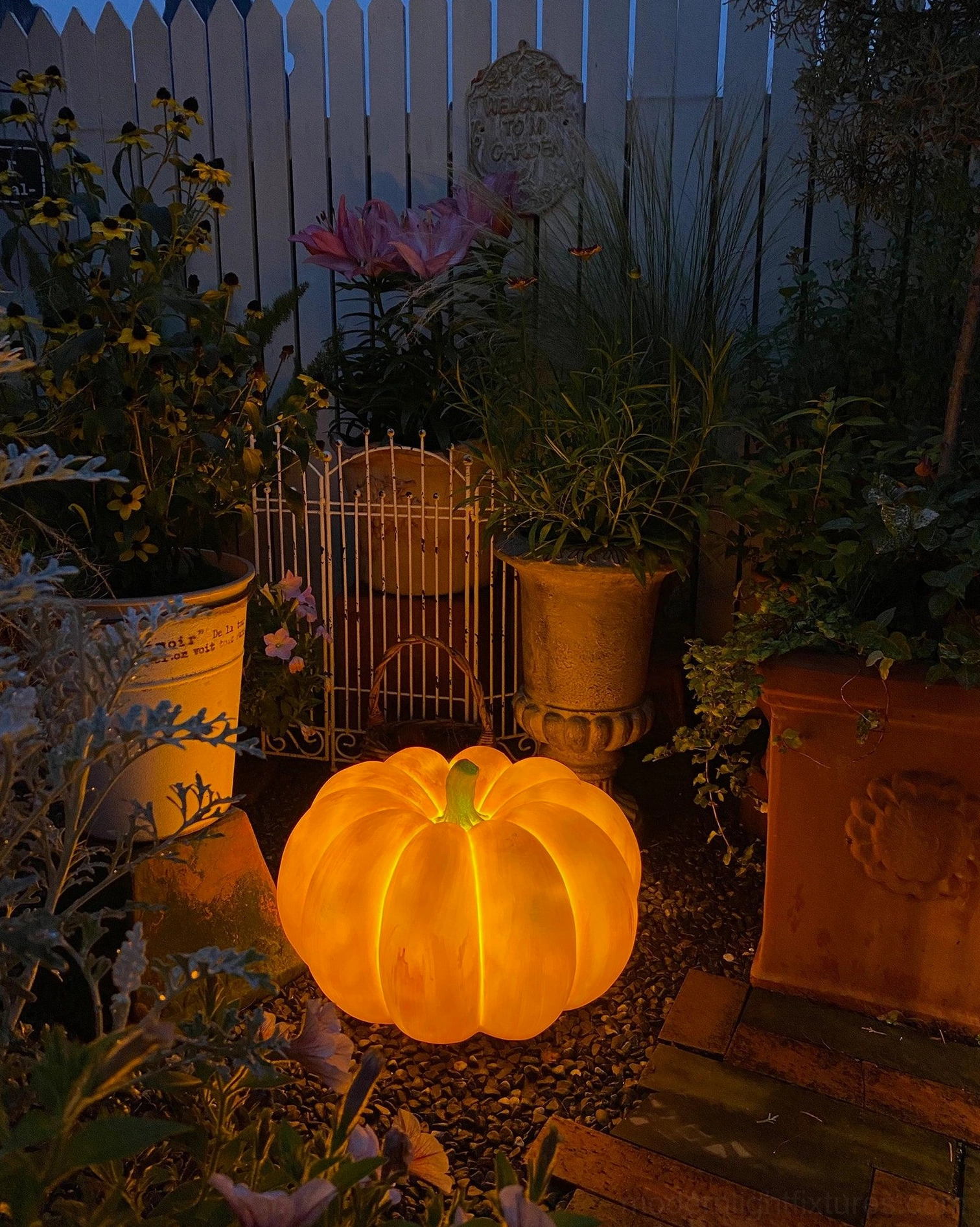 Glowing orange pumpkin outdoor lamp garden ground backyard fence evening ambient lighting