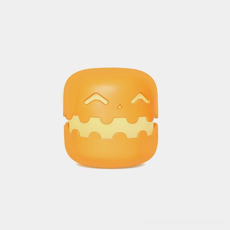 Whimsical orange pumpkin table lamp with squinting jack-o'-lantern face, front view on white background
