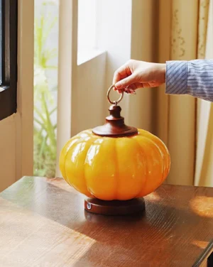 Amber pumpkin table lamp side view on wooden table by window with warm natural sunlight creating ambient glow in home interior