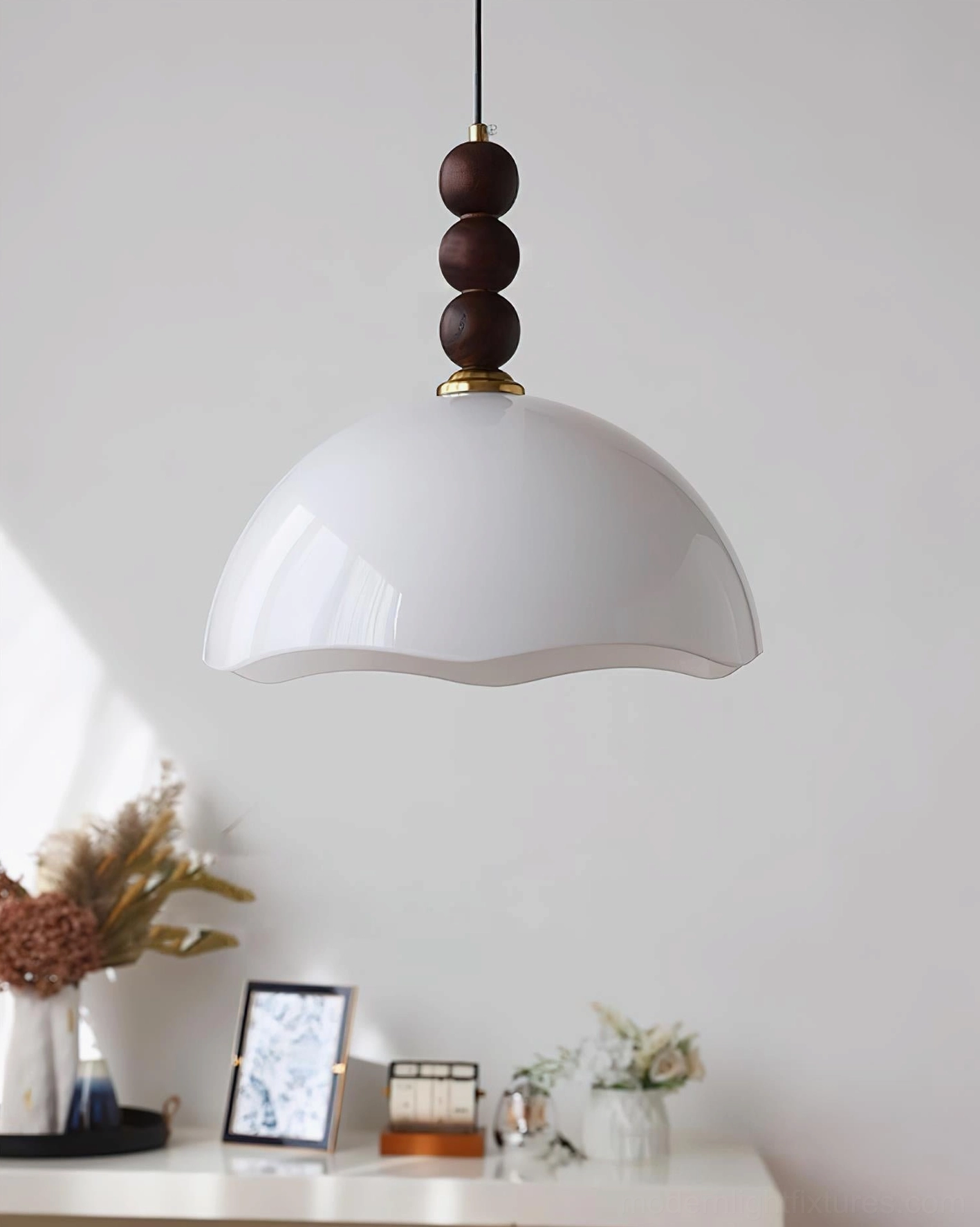 Side hanging view of pure white rippled glass pendant light with brass hardware and dark wood bead accent on console table