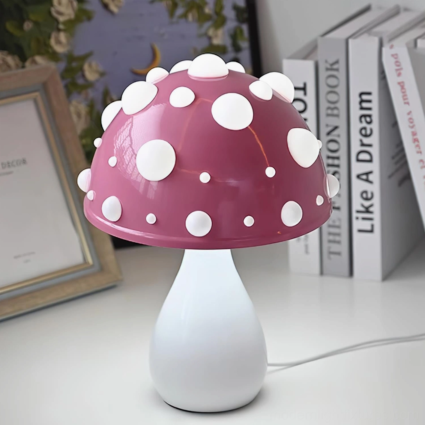 Purple spotted mushroom table lamp with matte cap and white stem on bookshelf desk, three-quarter view with book backdrop
