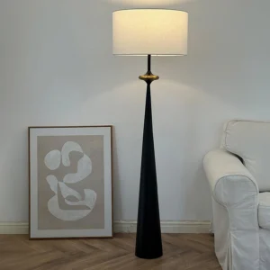 Modern black tapered floor lamp in minimalist living room setting with sofa and contemporary wall art