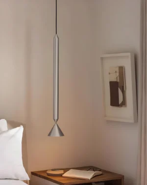 Silver Pylon pendant light installed in minimalist bedroom above bedside table, showing matte metallic finish and cone diffuser