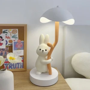 Rabbit hug table lamp in cozy bedroom bedside setting with cork board and bed in background