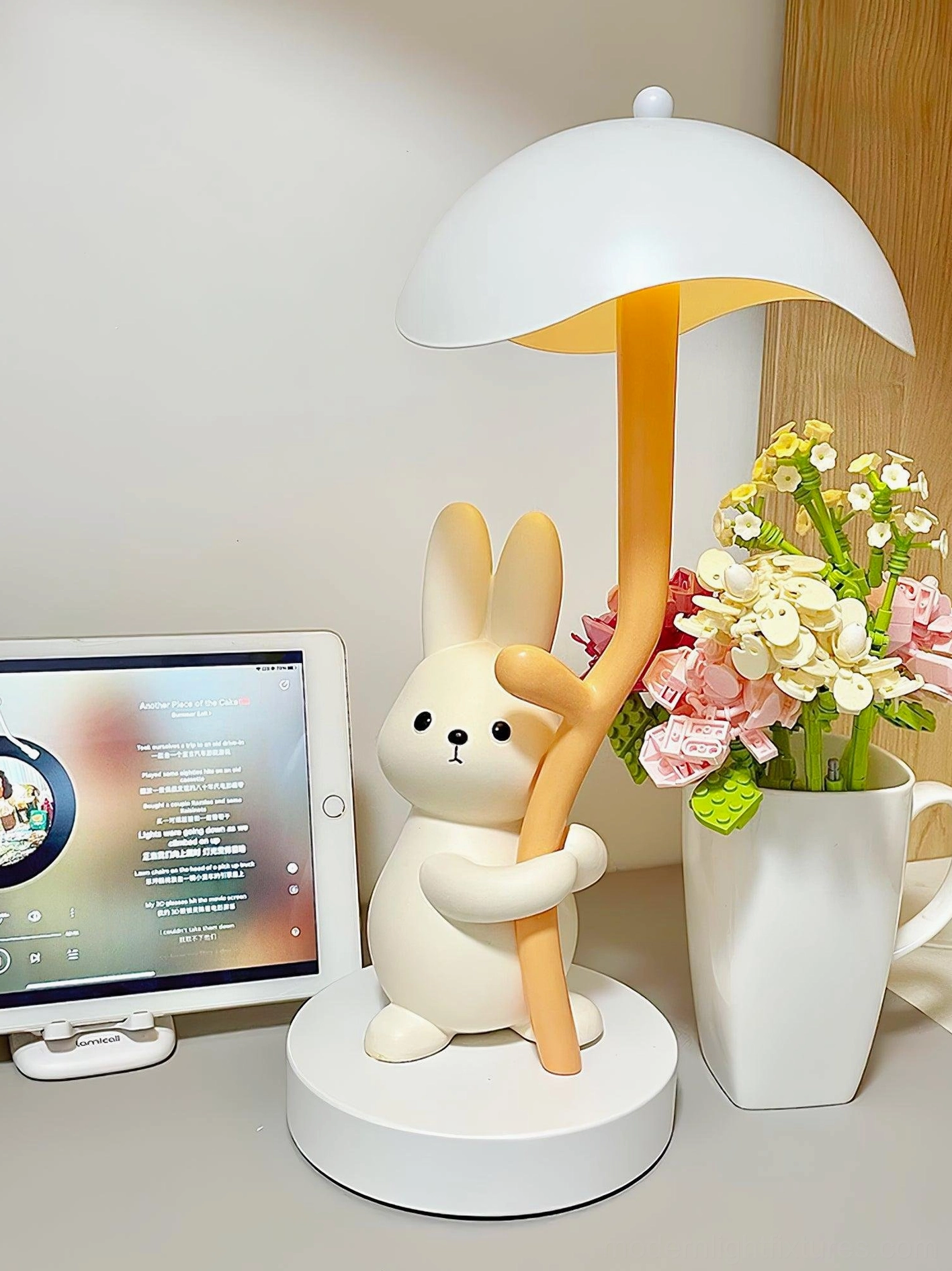 Rabbit hug table lamp three-quarter left side view with tablet and flower vase on desk