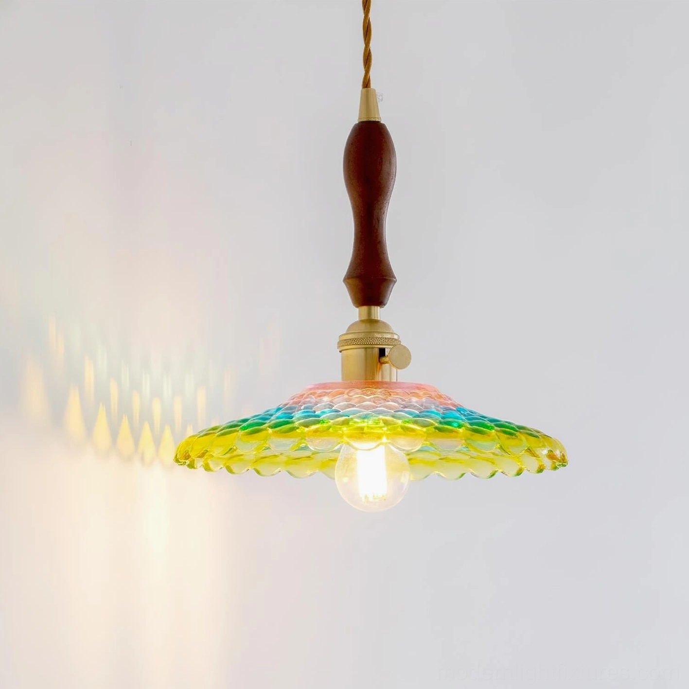 Three-quarter view of Rainbowa pendant lamp showing honeycomb textured glass shade casting colorful light patterns on wall