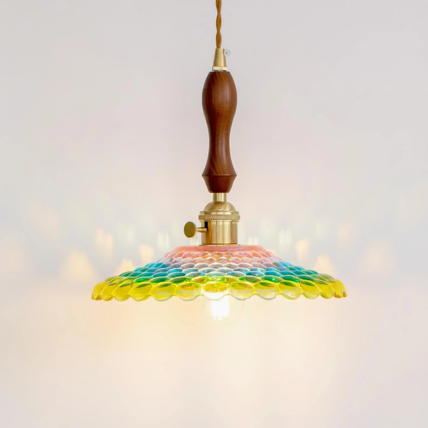 Front low-angle view of Rainbowa pendant light with warm glowing exposed bulb against studio background