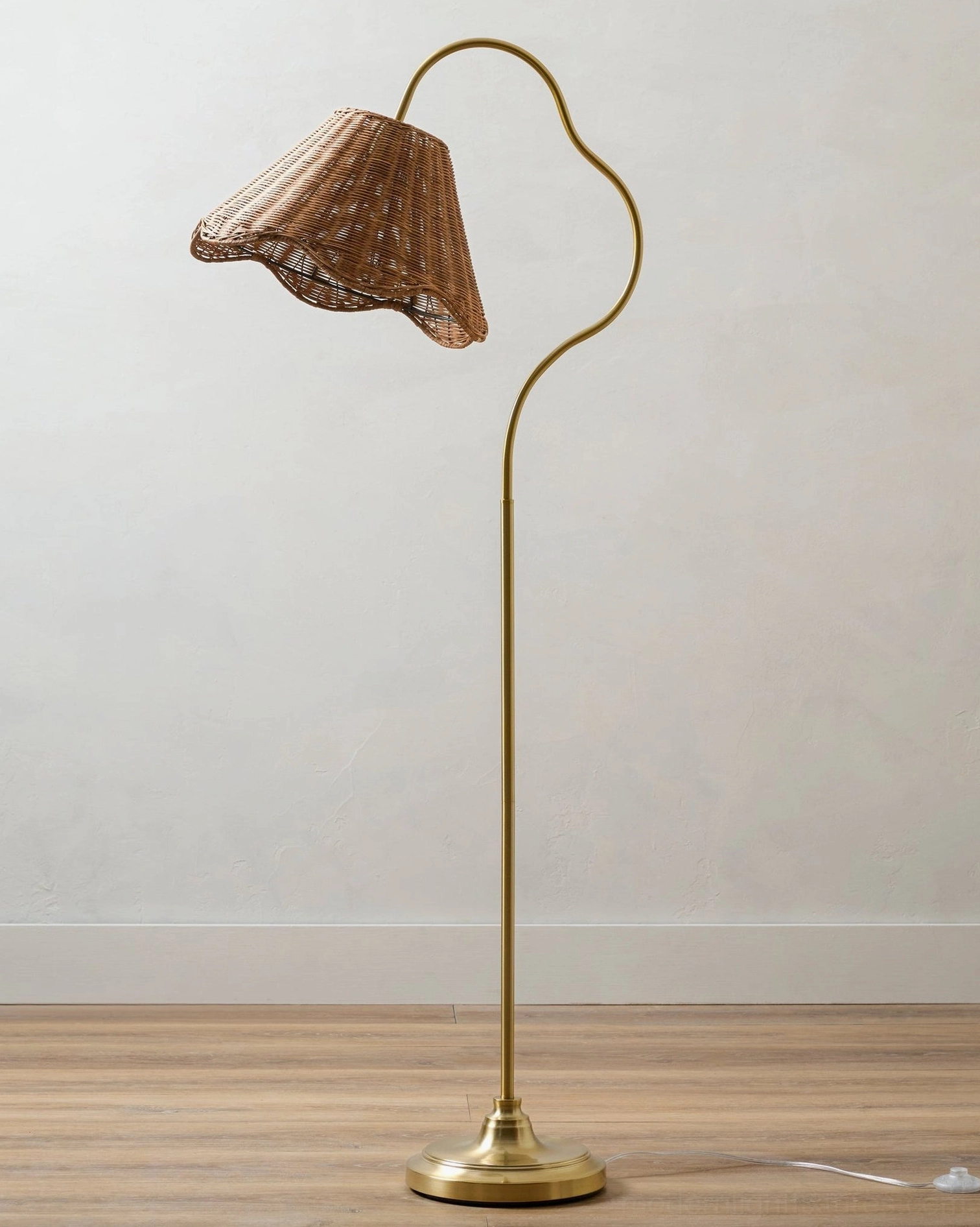 Arc floor lamp on wooden floor showing brass metal base and curved stem with natural woven rattan shade