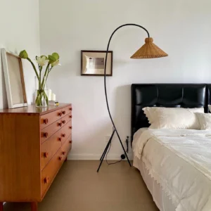 Woven rattan arc floor lamp in bedroom setting with curved metal pole and natural bell-shaped shade