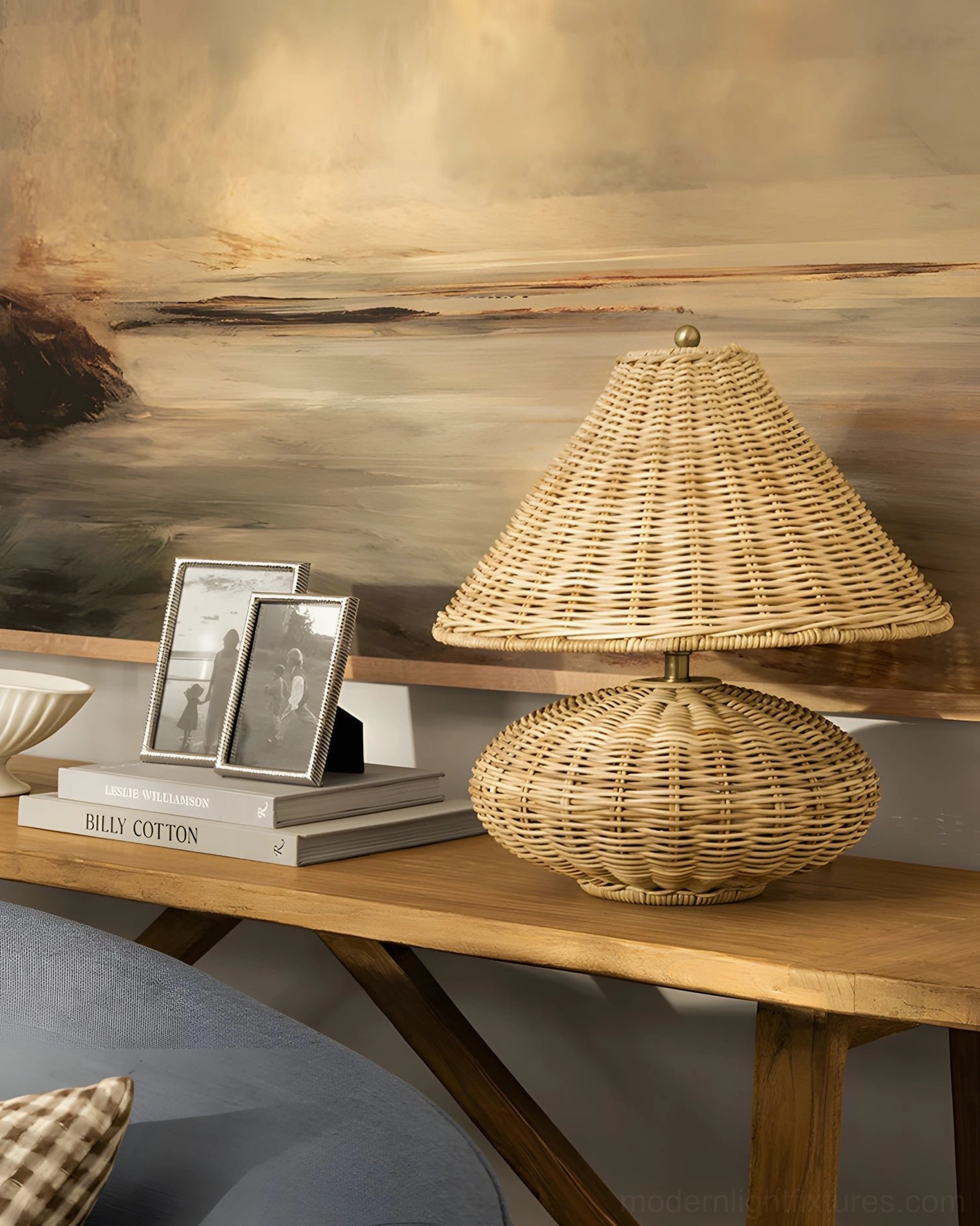 Handwoven rattan lamp on living room side table with photo frames and stacked books, artistic oblique perspective showing boho styling