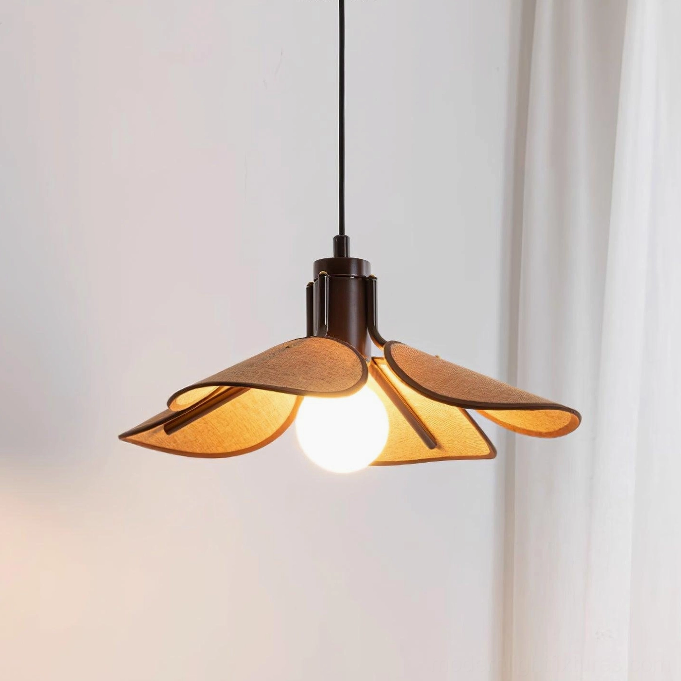 Modern boho rattan pendant light with petal-shaped shade, three-quarter front view against white curtain backdrop
