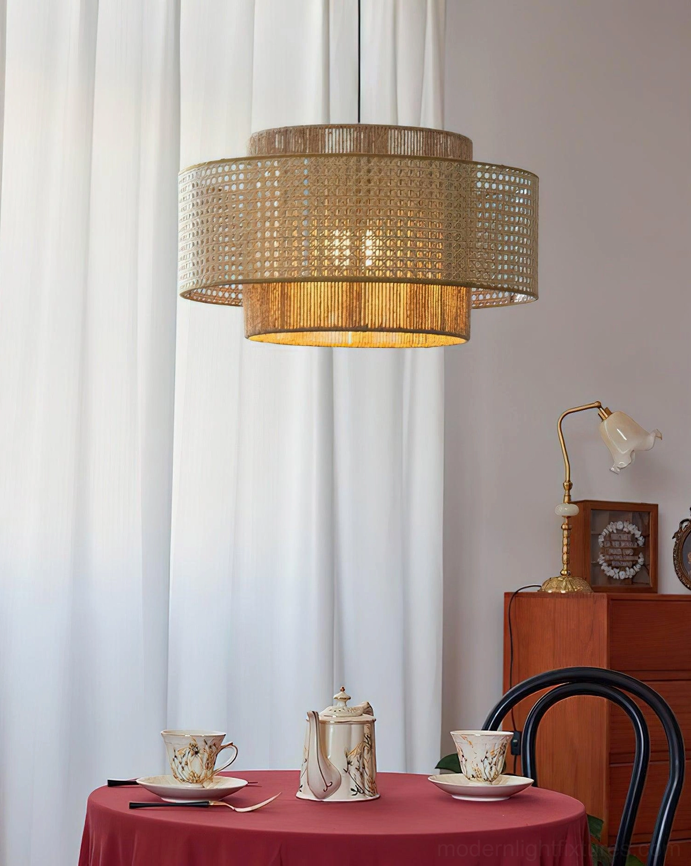 Rattan pendant light fixture in home dining room with warm red tablecloth, wooden cabinet and complementary table lamp styling